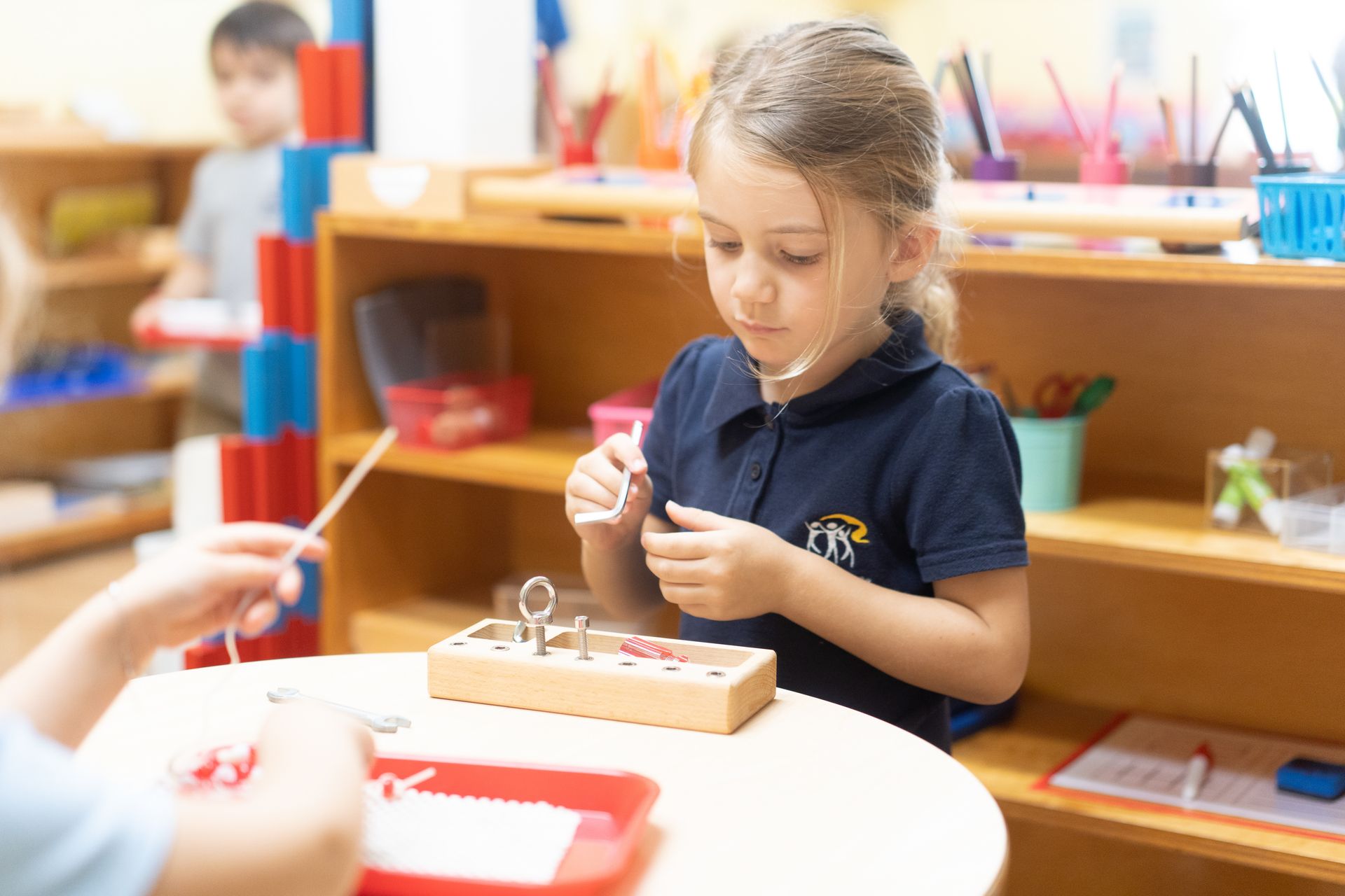 A Montessori child is sitting at a table working with practical life material.