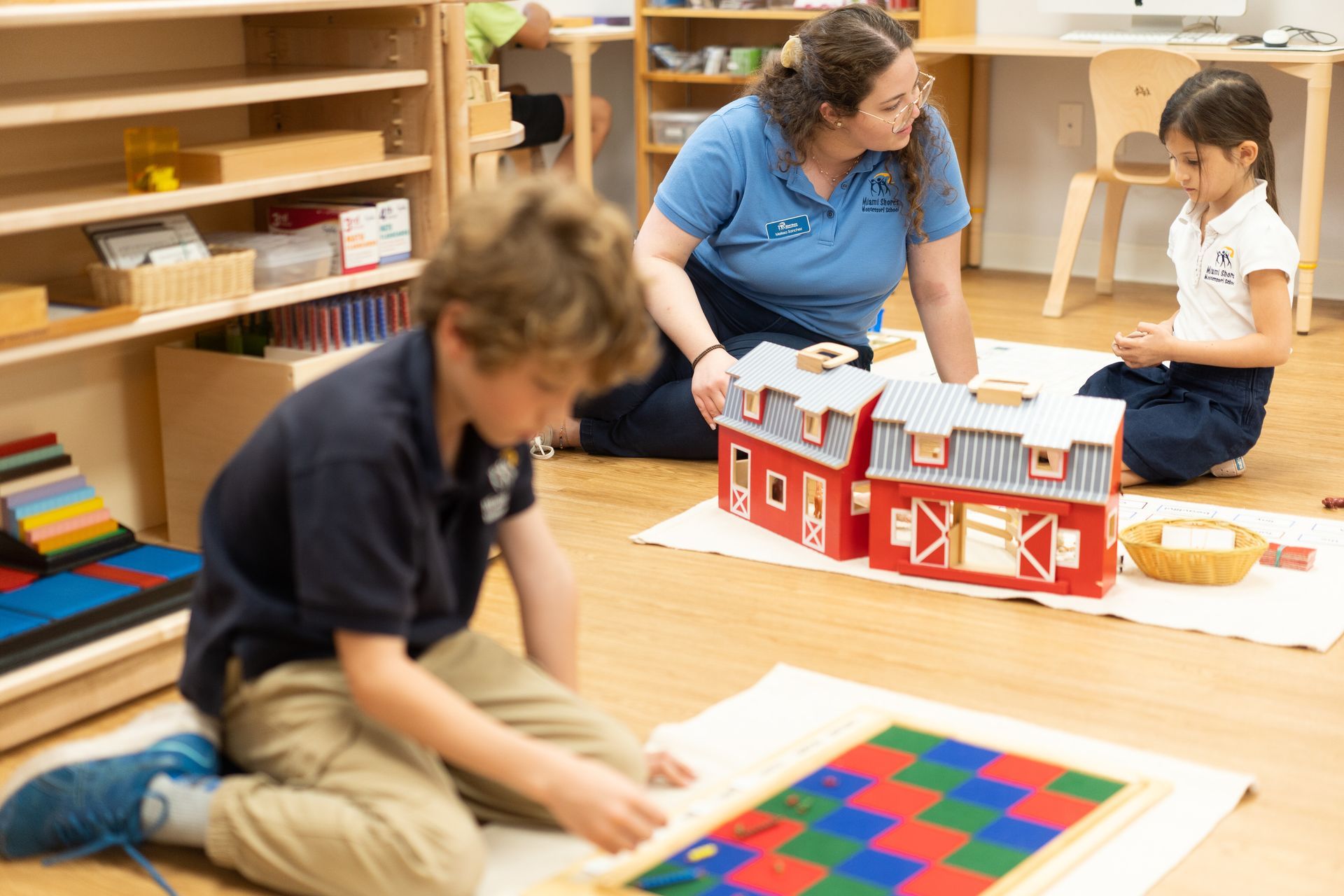 A Montessori guide and children are sitting on the floor working with materials.
