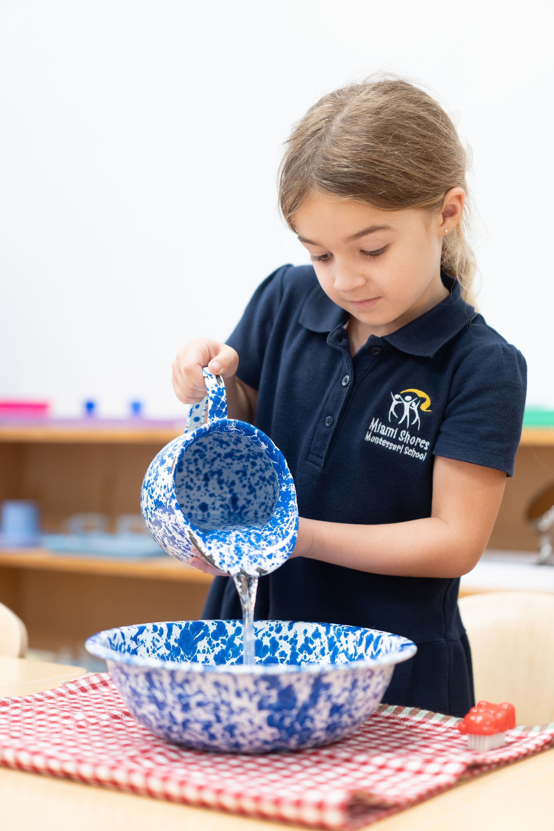 A Montessori child is pouring water into a bowl.