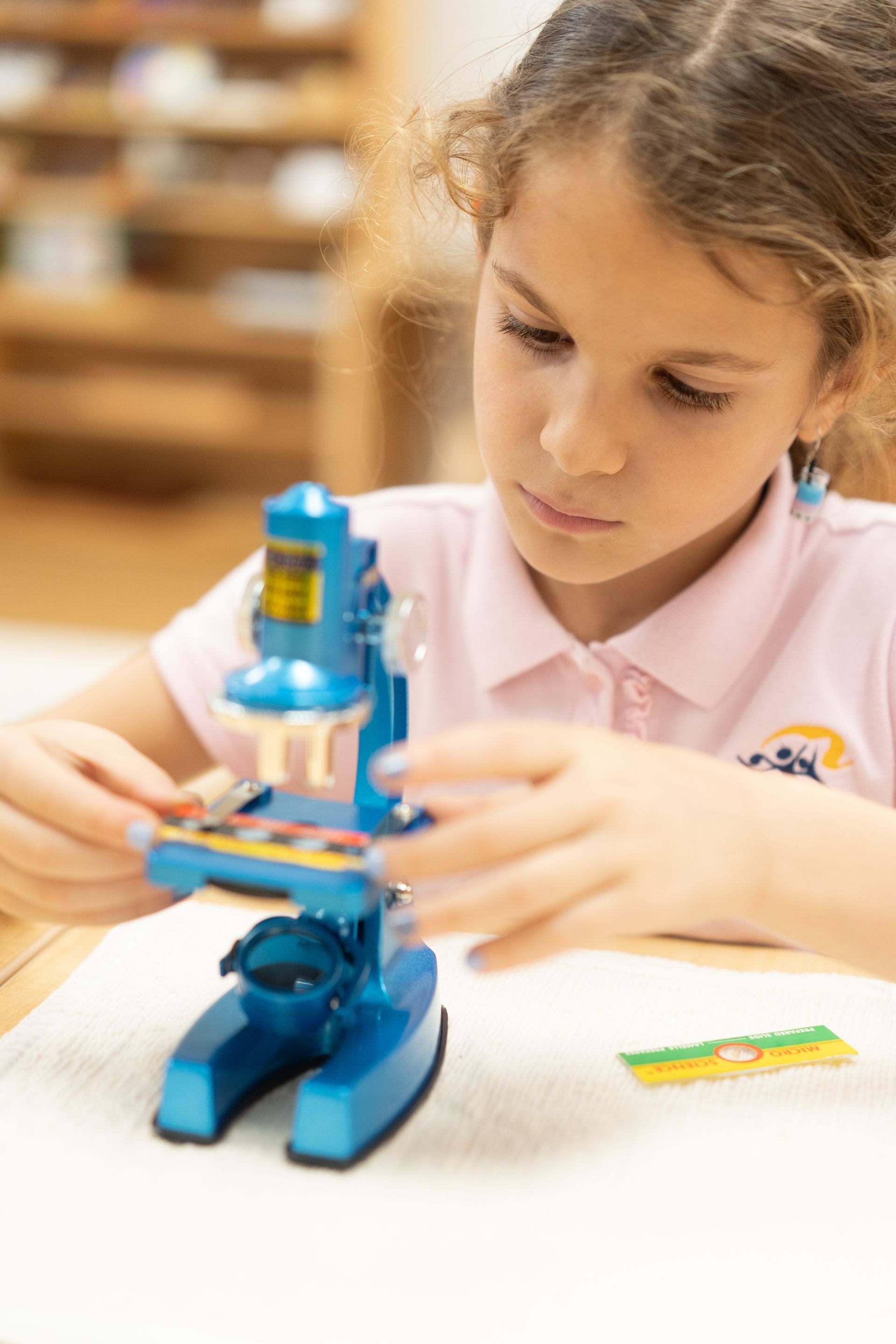 A Montessori child is sitting at a table looking through a microscope.