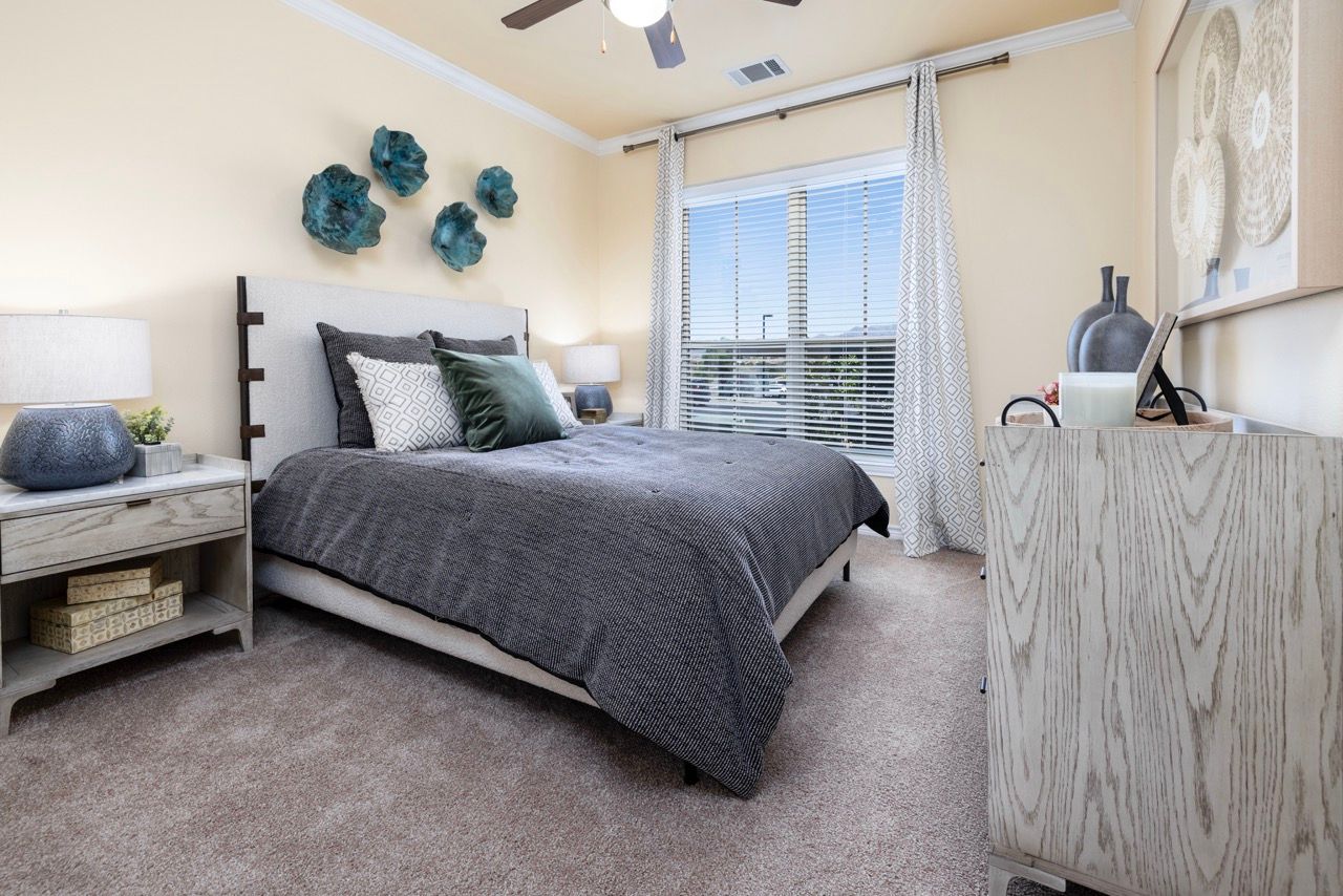 Bedroom in a modern apartment with a bed, two nightstands, dresser, and window blinds.