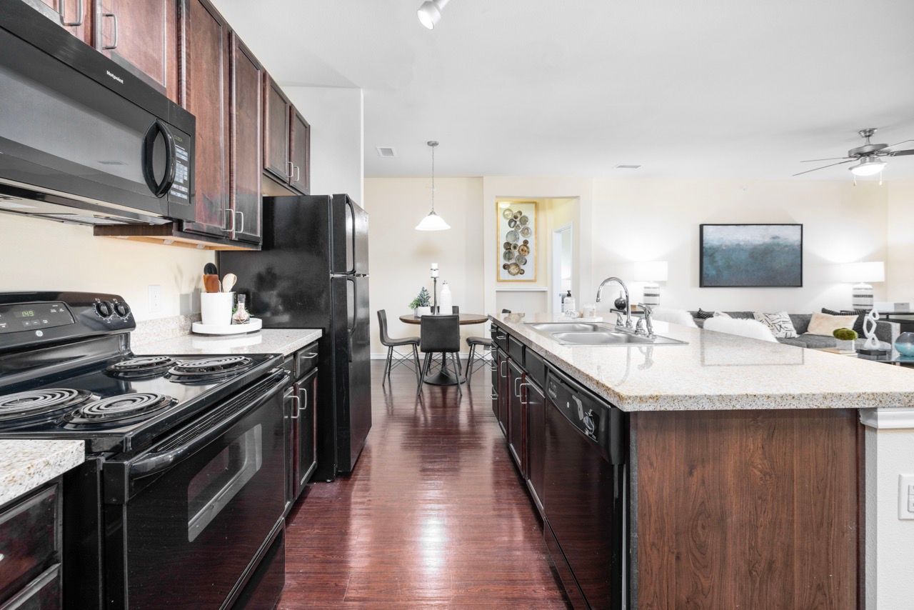 Modern kitchen with dark wood cabinets, black appliances, and a large island.