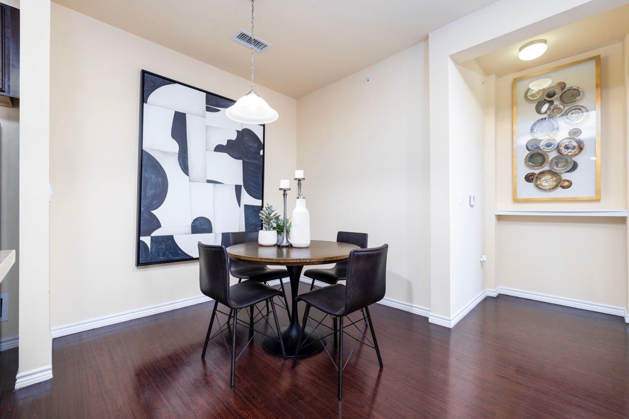 Dining area with round table and four black chairs, abstract wall art, dark wood floor.