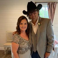 A man wearing a cowboy hat and glasses is standing next to a woman in a dress.