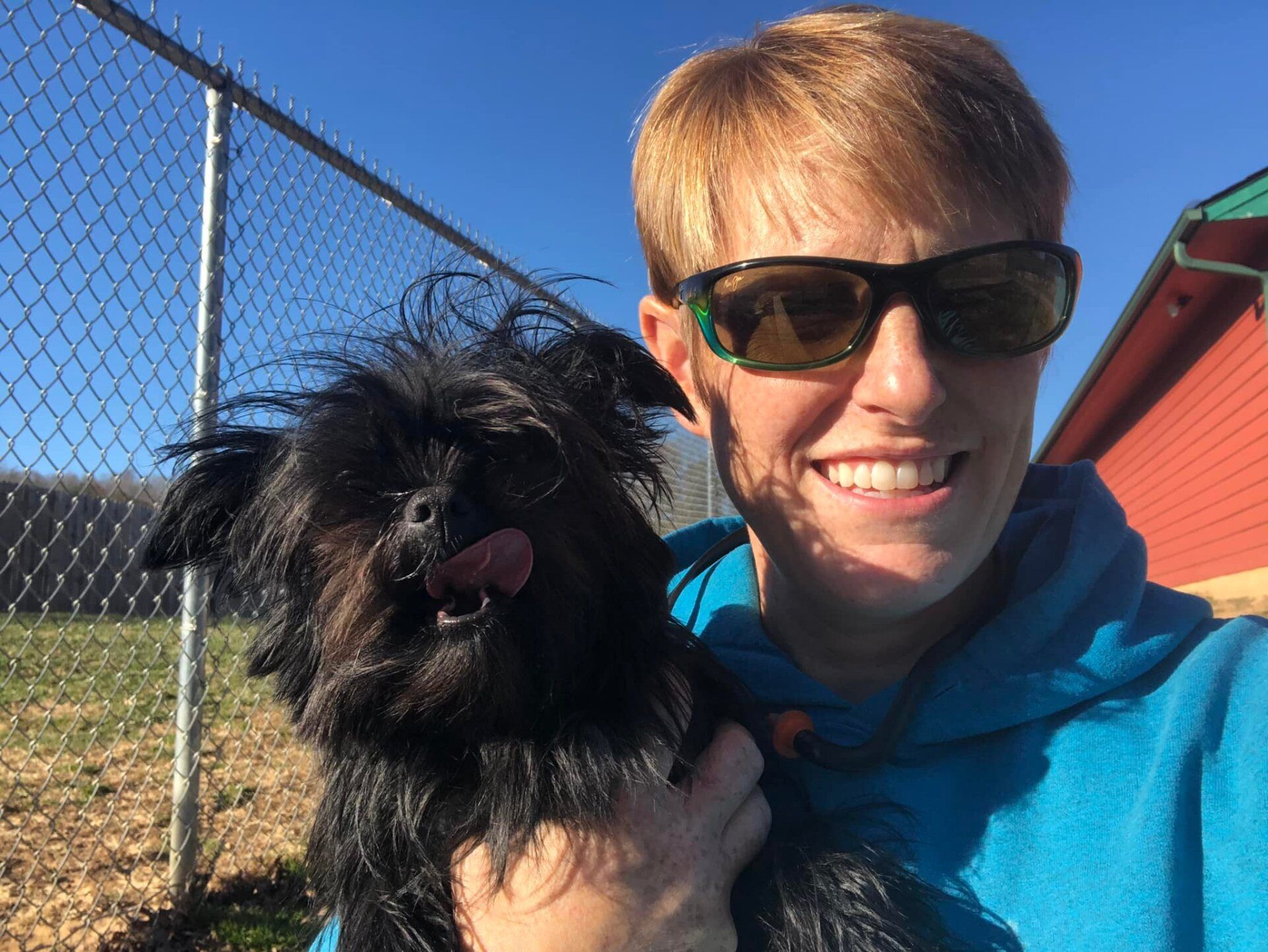 A woman wearing sunglasses is holding a small black dog