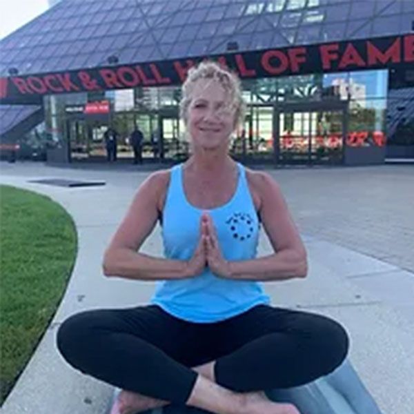 A woman is sitting in a lotus position in front of a rock & roll hall of fame building.