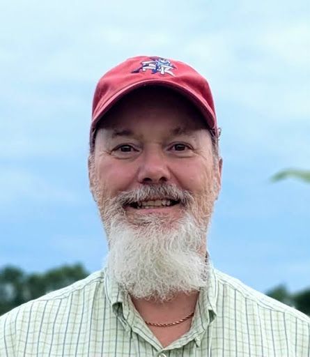 A man with a beard and a red hat is smiling for the camera.