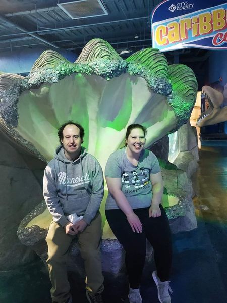 A man and a woman are posing for a picture in front of a sign that says caribbean.