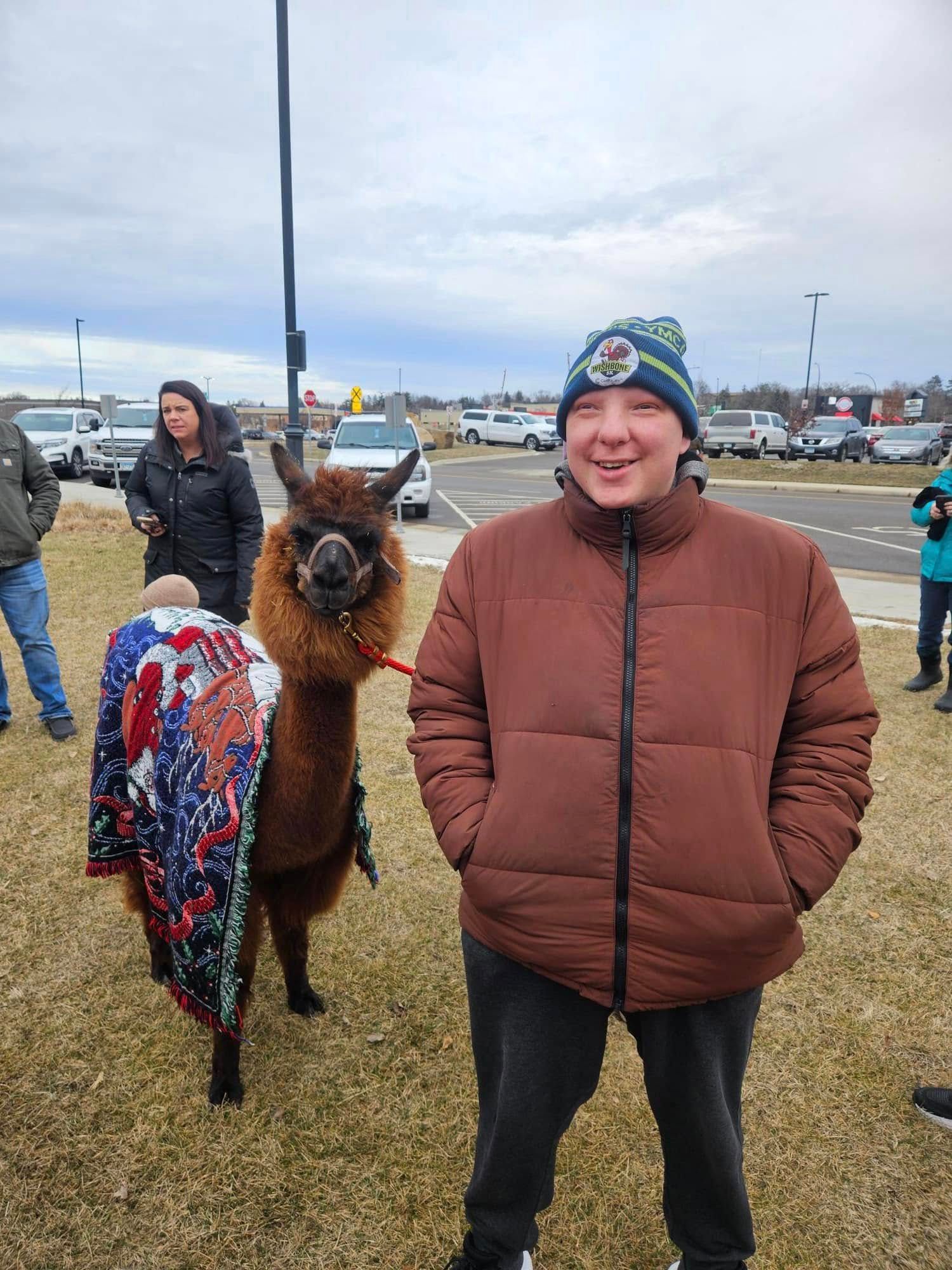 A man is standing next to a llama in a parking lot.