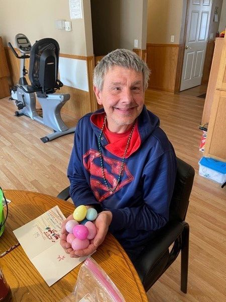 A man in a superman sweatshirt is sitting at a table holding easter eggs.
