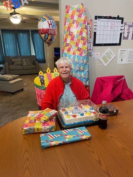 A woman is sitting at a table with a birthday cake and a coca cola bottle.