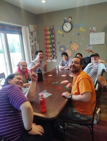 A group of people are sitting around a table with a clock on the wall behind them.