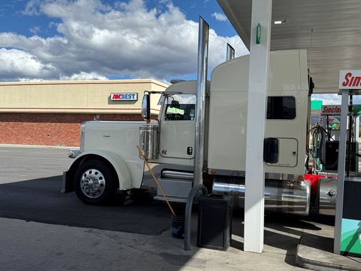 Cream-colored semi-truck at a gas station fueling up, under a cloudy sky.