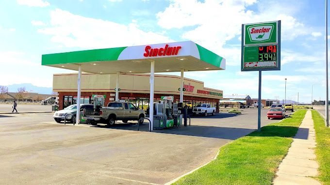 Sinclair gas station with green and white canopy, parked cars, gas prices displayed.