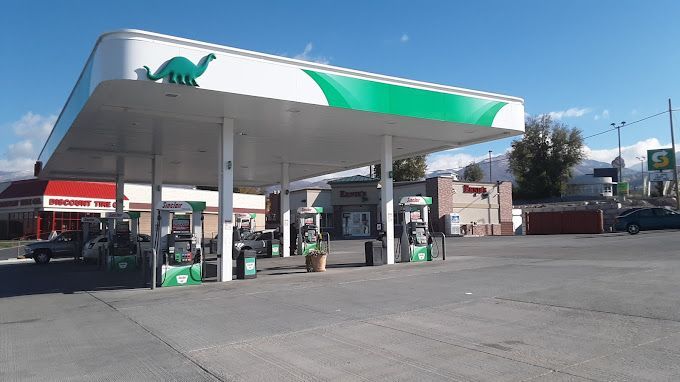 Dino Mart gas station with green and white canopy, pumps, and dinosaur logo.