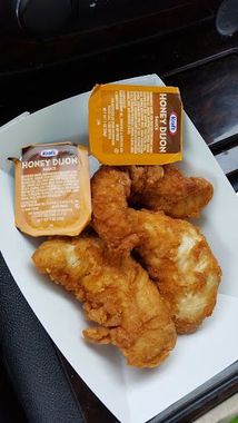 Fried chicken tenders and two packets of Kraft Honey Dijon sauce in a paper tray.