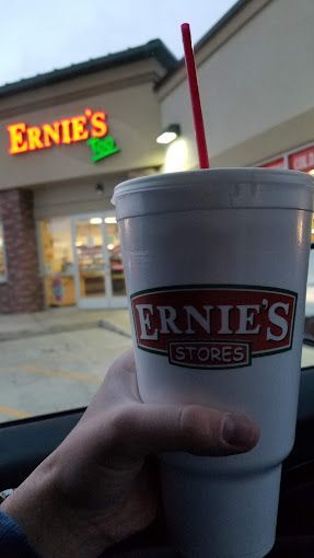 Hand holding a large Ernie's Stores cup with a red straw, store sign in the background.