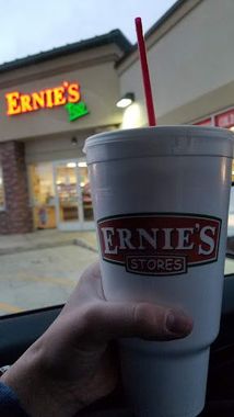 Hand holding a large Ernie's Stores cup with a red straw, store sign in the background.