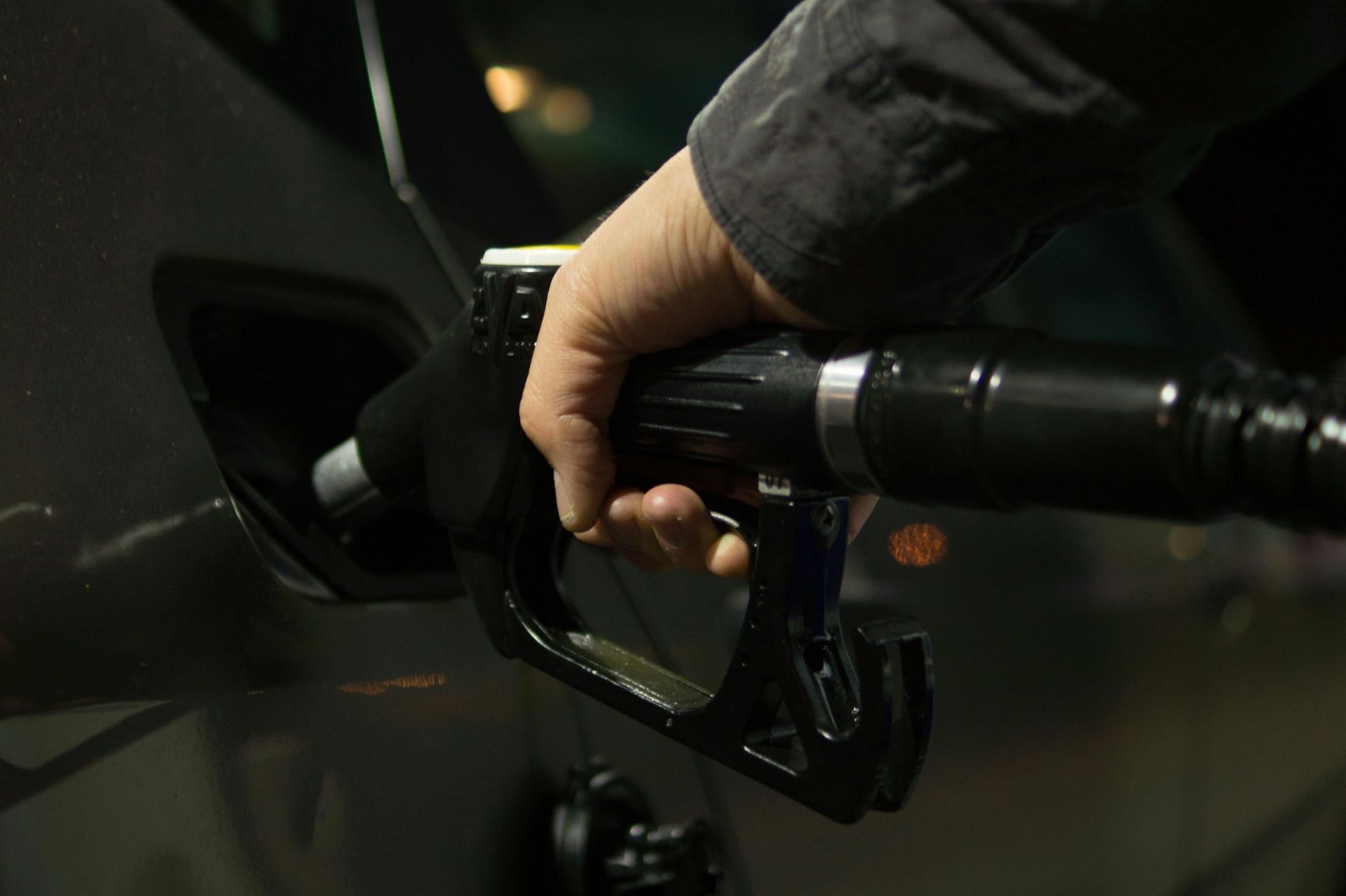 Hand holding a gas pump nozzle, refueling a car at a gas station.