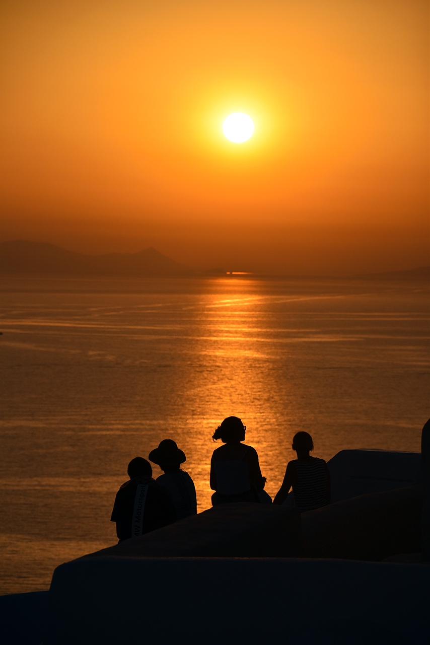 A group of people are sitting on a rock overlooking the ocean at sunset.