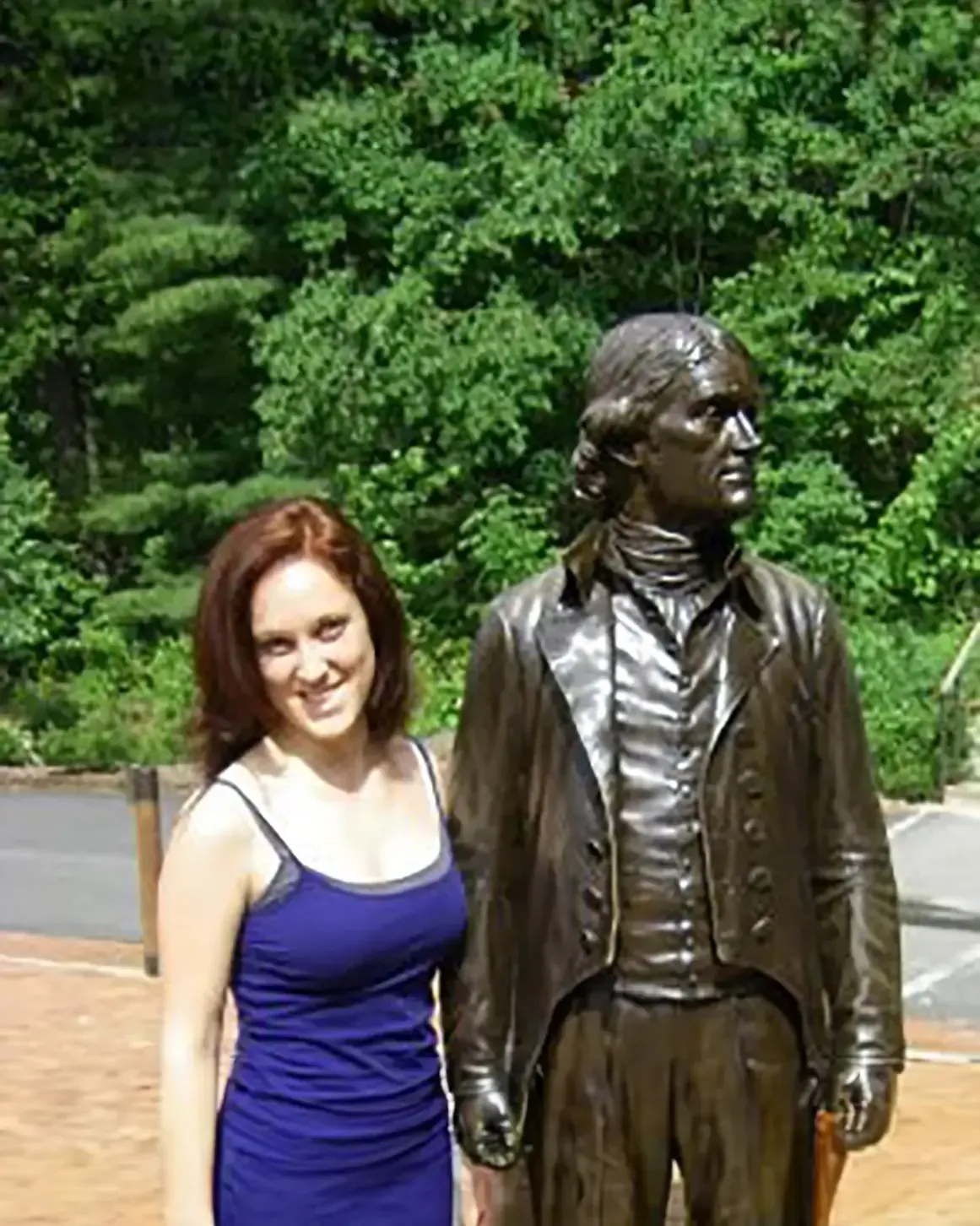 A woman is standing next to a statue of a man in a suit.