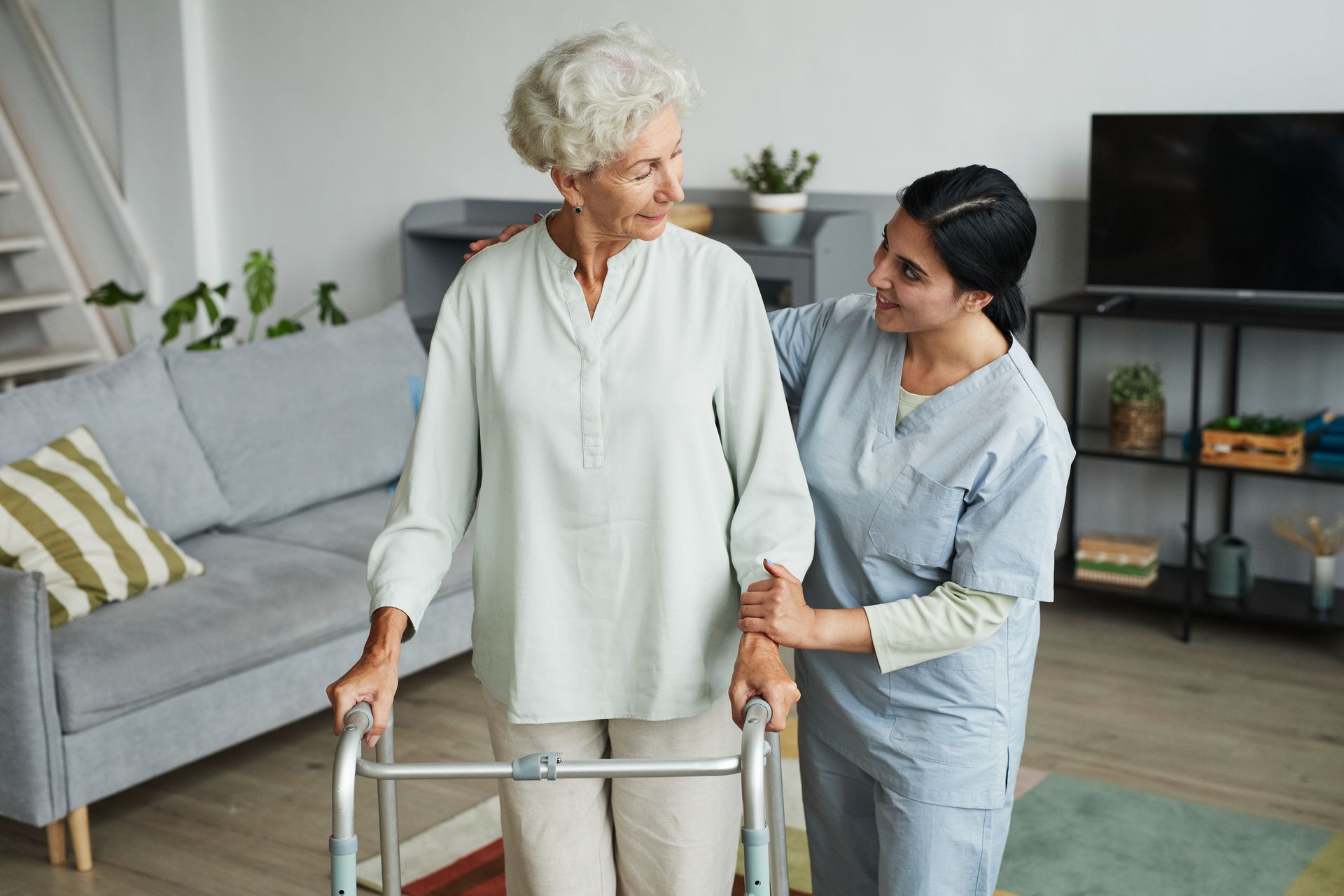 A caregiver gently assists a person using a walker in a living room.