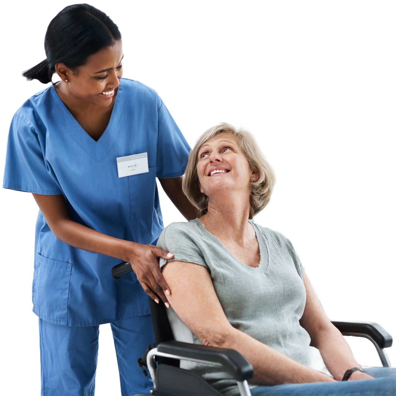 A healthcare worker in blue scrubs smiles while assisting a person seated in a wheelchair.