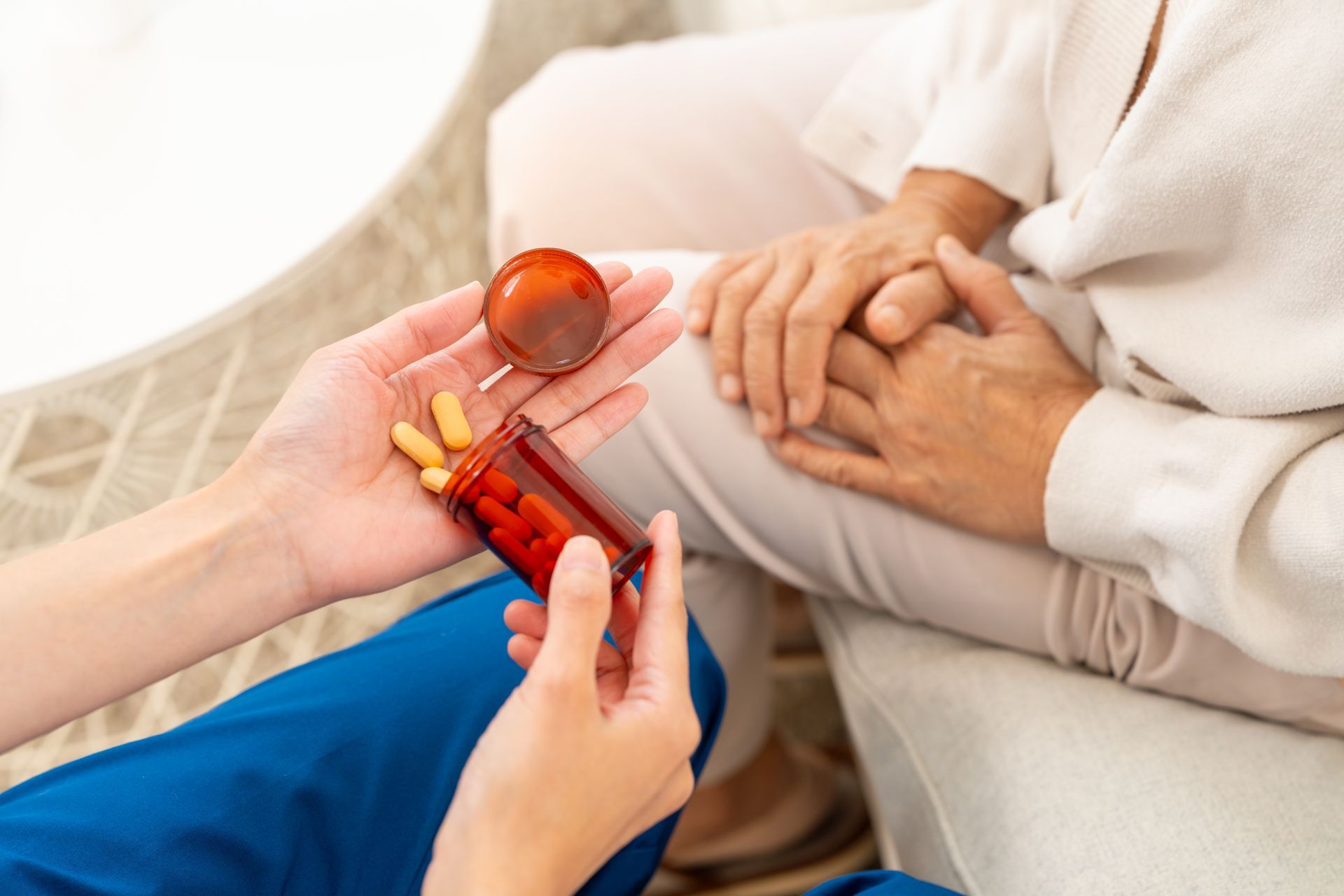 A person in blue scrubs pours yellow capsules from a brown pill bottle into another person’s open palm.