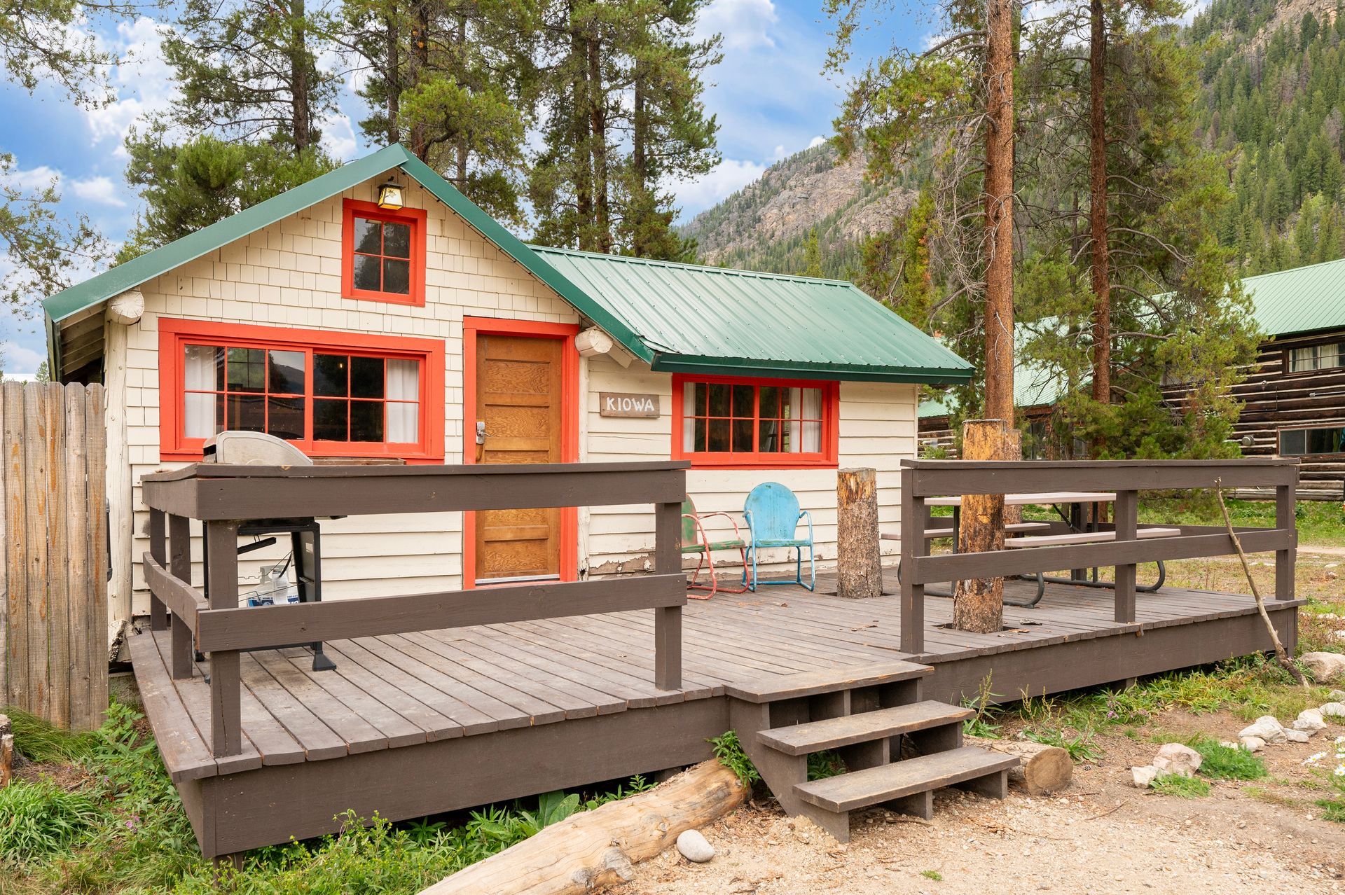 A small white house with a green roof and a wooden deck.