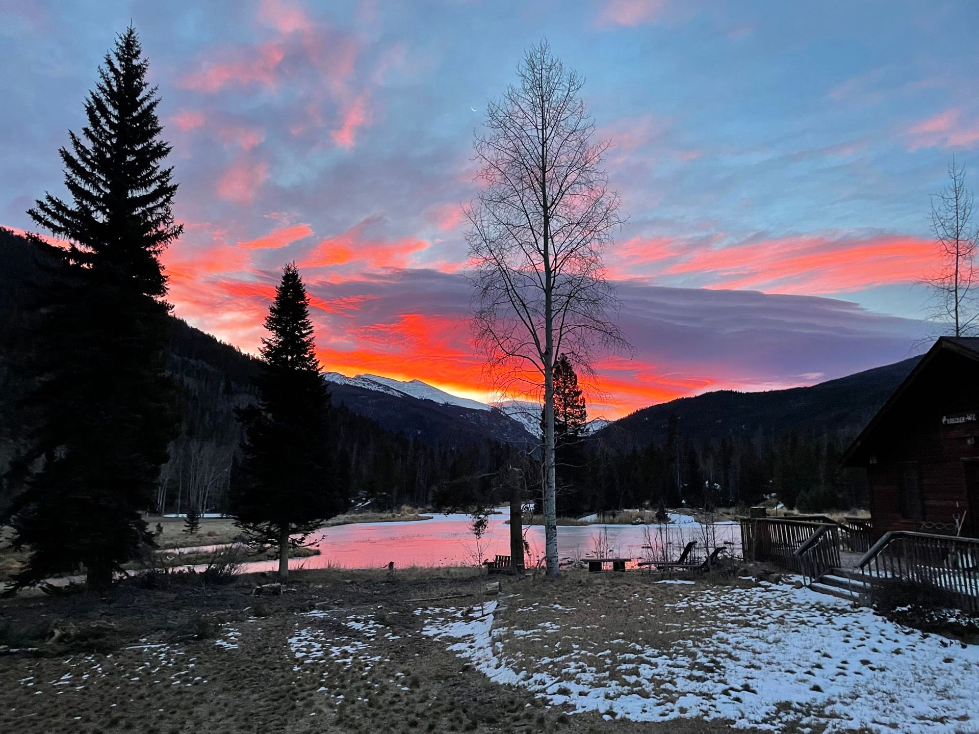 A sunset over a lake with trees in the foreground and mountains in the background