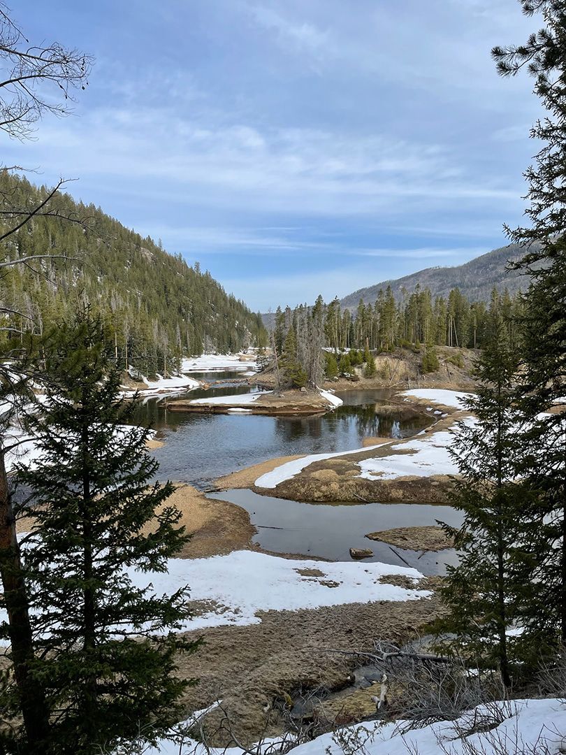 A lake in the middle of a snowy valley surrounded by trees.