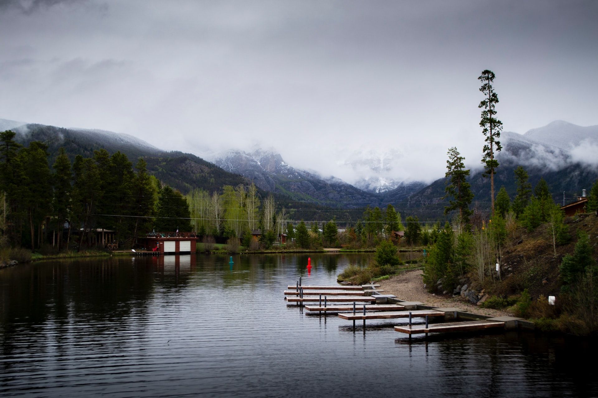 A lake with a dock and mountains in the background on a cloudy day.