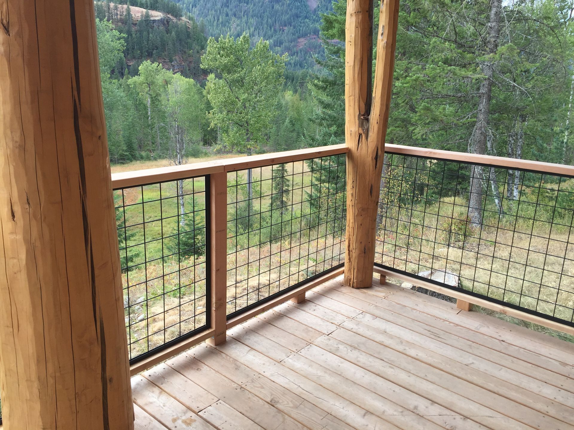 A wooden deck with a metal railing and trees in the background.