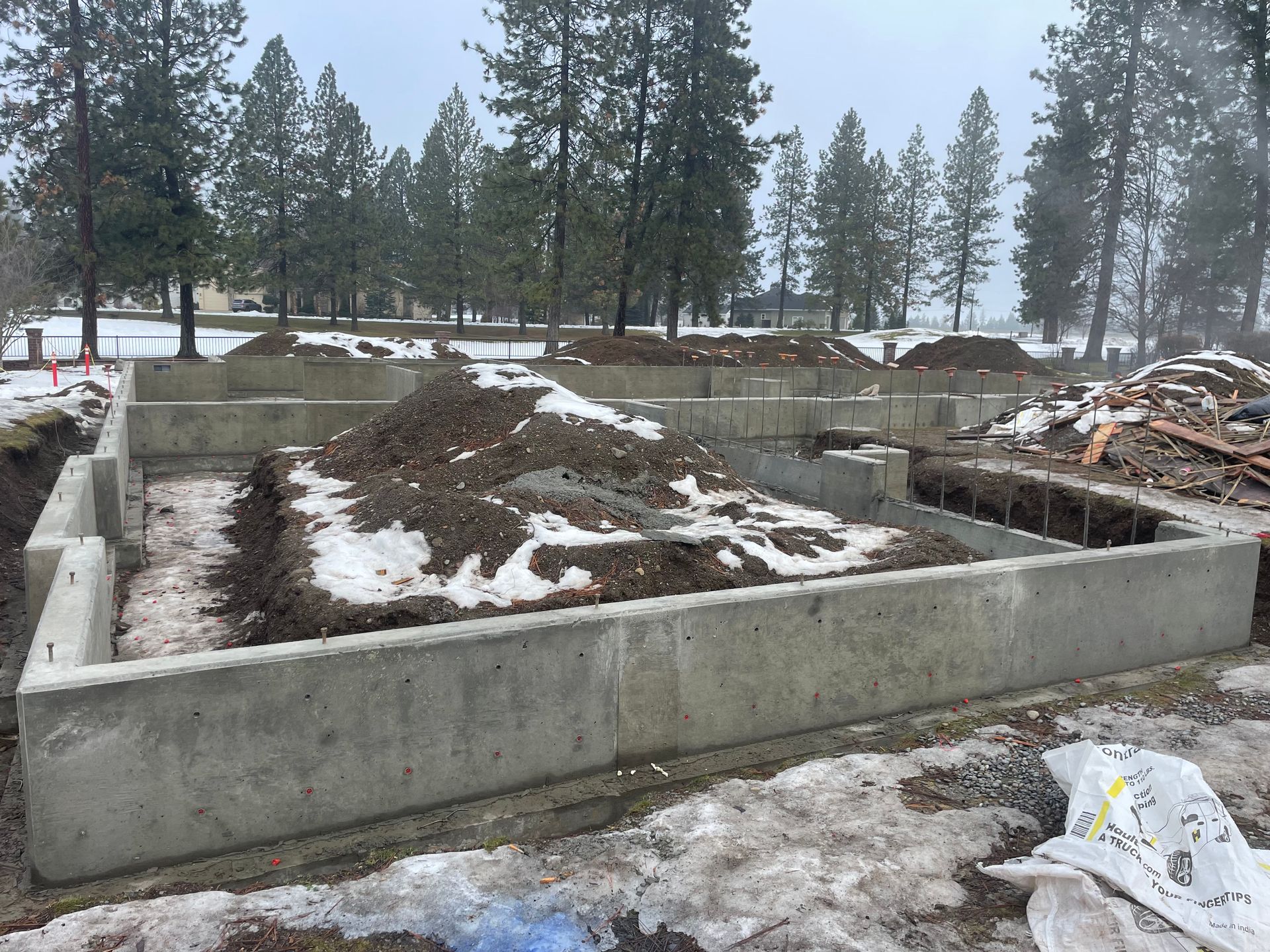 A concrete foundation is being built in the snow with trees in the background.