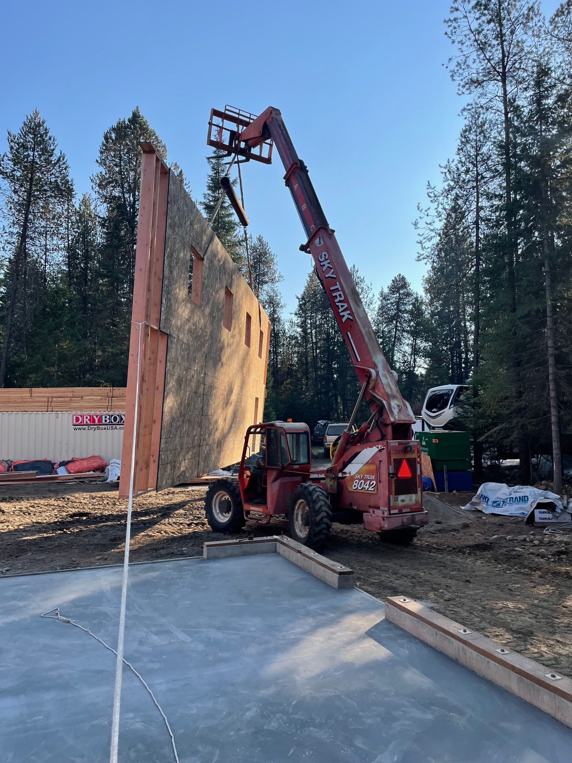 A red crane is lifting a large piece of wood on a construction site.