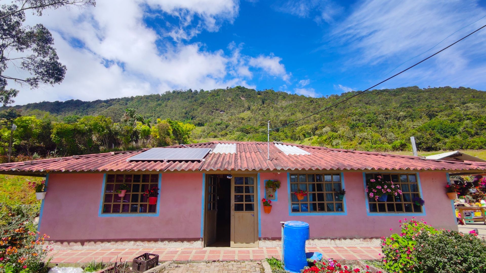 Una casa rosa con techo rojo está rodeada de montañas y árboles.