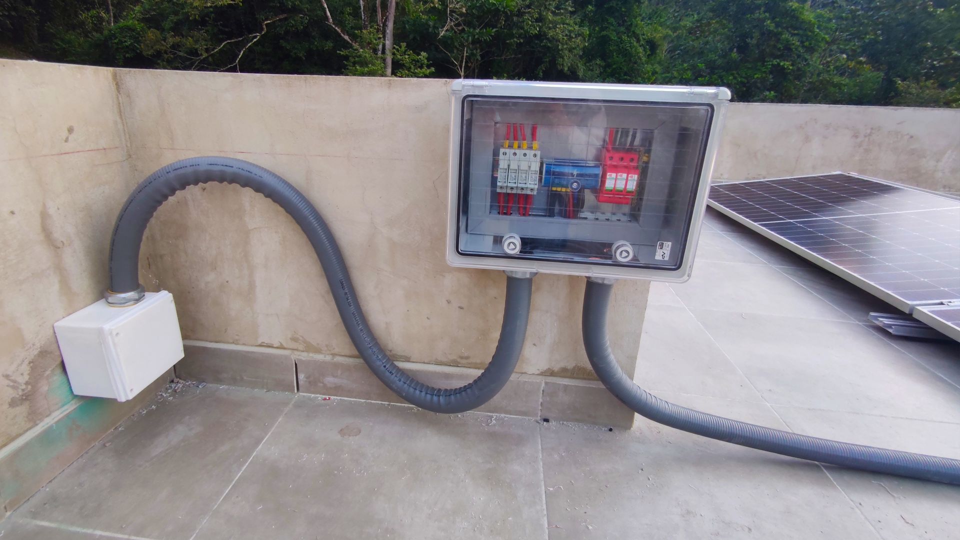 Una caja con una manguera conectada a ella está situada al lado de un panel solar.
