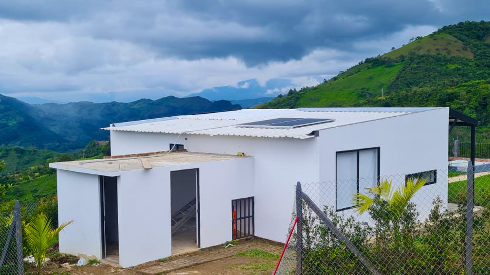 Una casa blanca está situada en la cima de una colina con montañas al fondo.