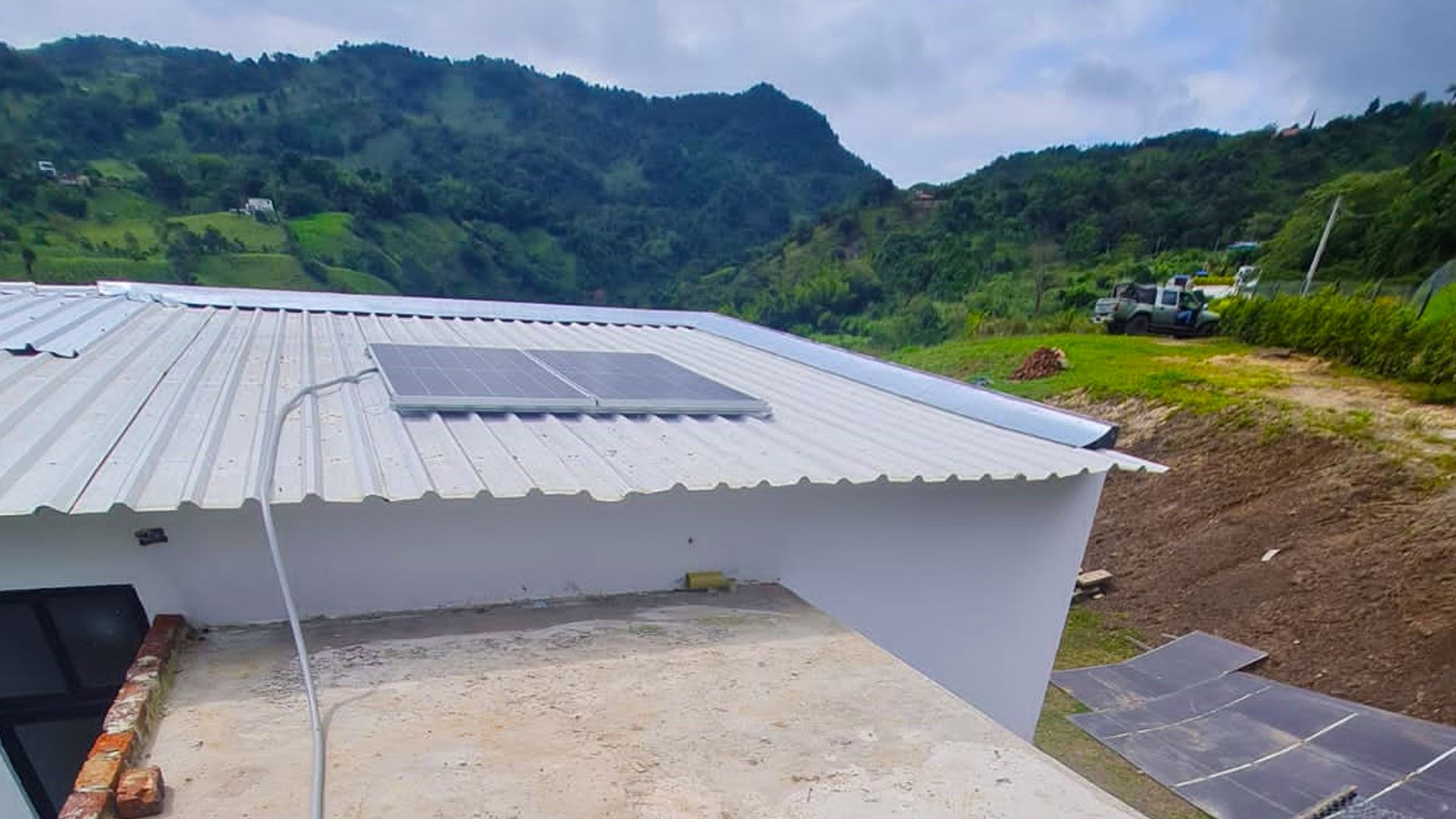 Una casa blanca con paneles solares en el techo y montañas al fondo.