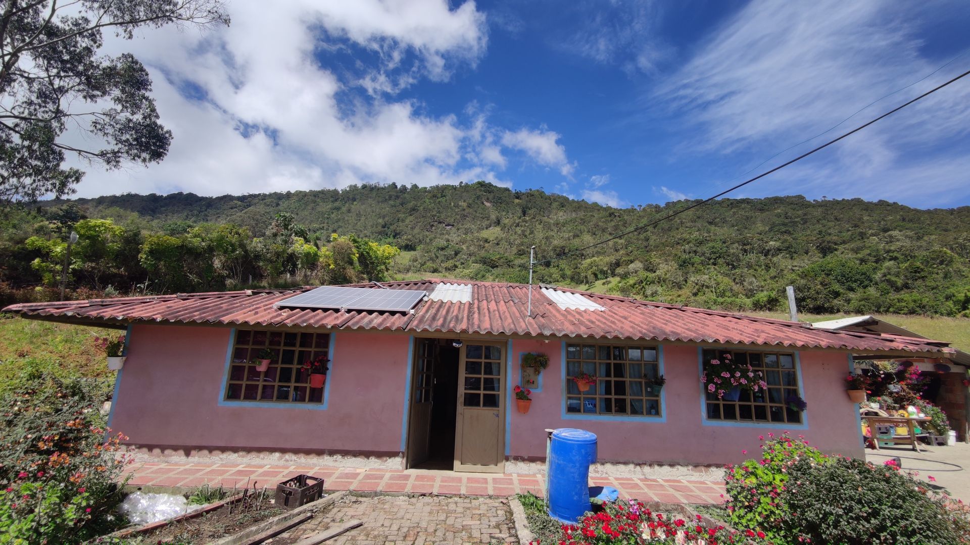 Una casa rosa con techo rojo está rodeada de árboles y montañas.