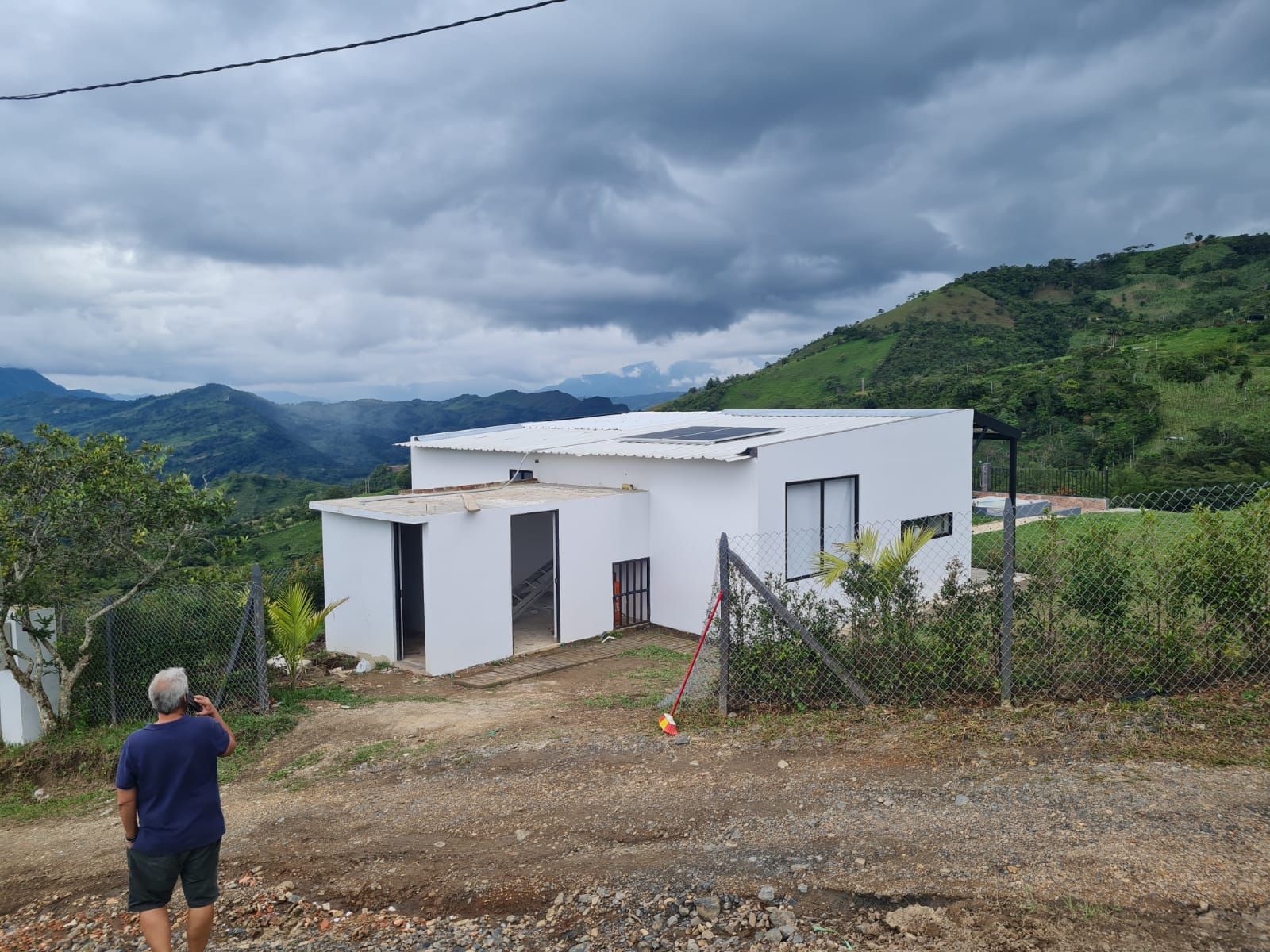 Un hombre está parado frente a una casa blanca con montañas al fondo.