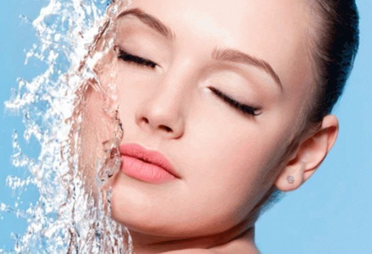 Un primer plano de la cara de una mujer con agua salpicándola.