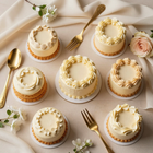 Surtido de mini pasteles de crema con detalles dorados sobre una mesa beige, rodeados de flores y cubiertos dorados.