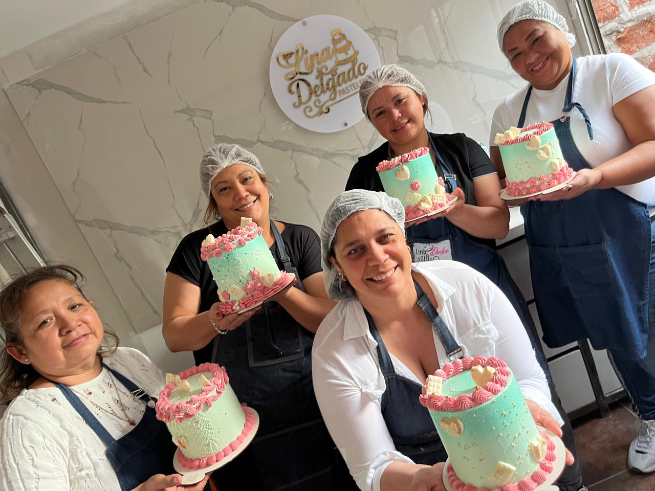 Cinco personas con redecillas para el cabello sostienen pasteles decorados en la cocina de una pastelería.