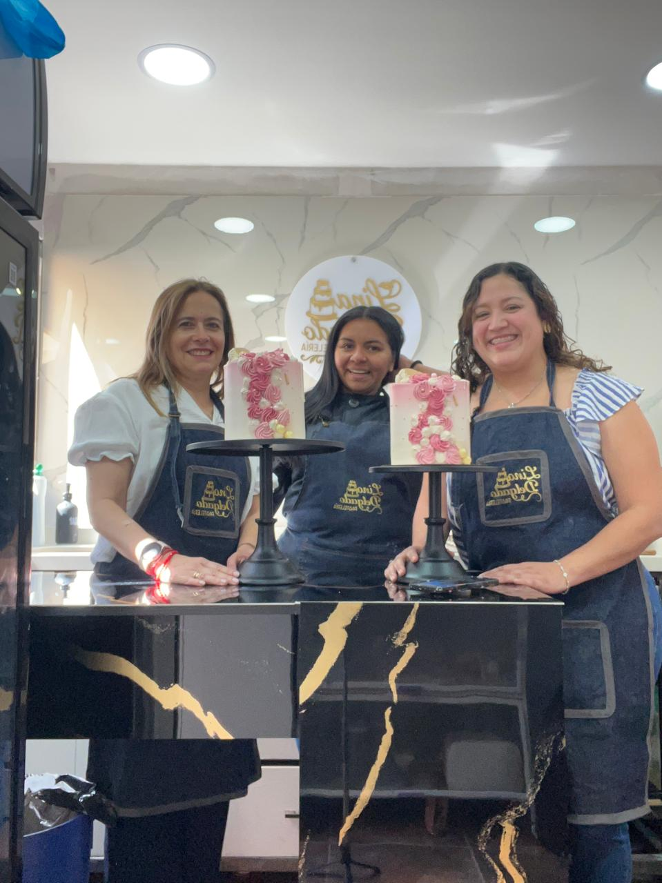 Tres personas sonriendo detrás de un mostrador, sosteniendo bolsas de regalo con flores en una tienda luminosa.
