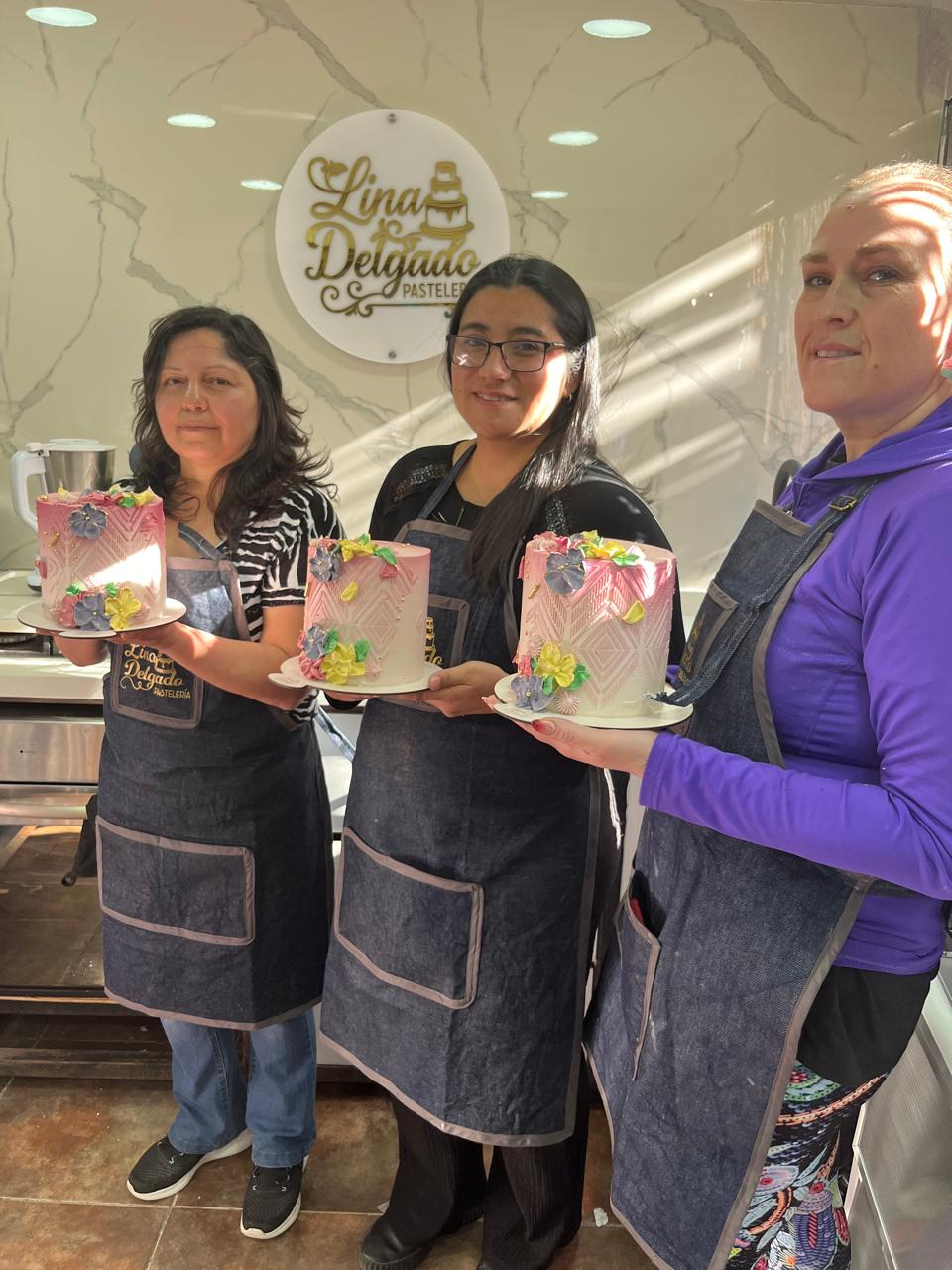 Tres panaderos con delantales sosteniendo cajas de pasteles decoradas dentro de la fachada de una panadería.