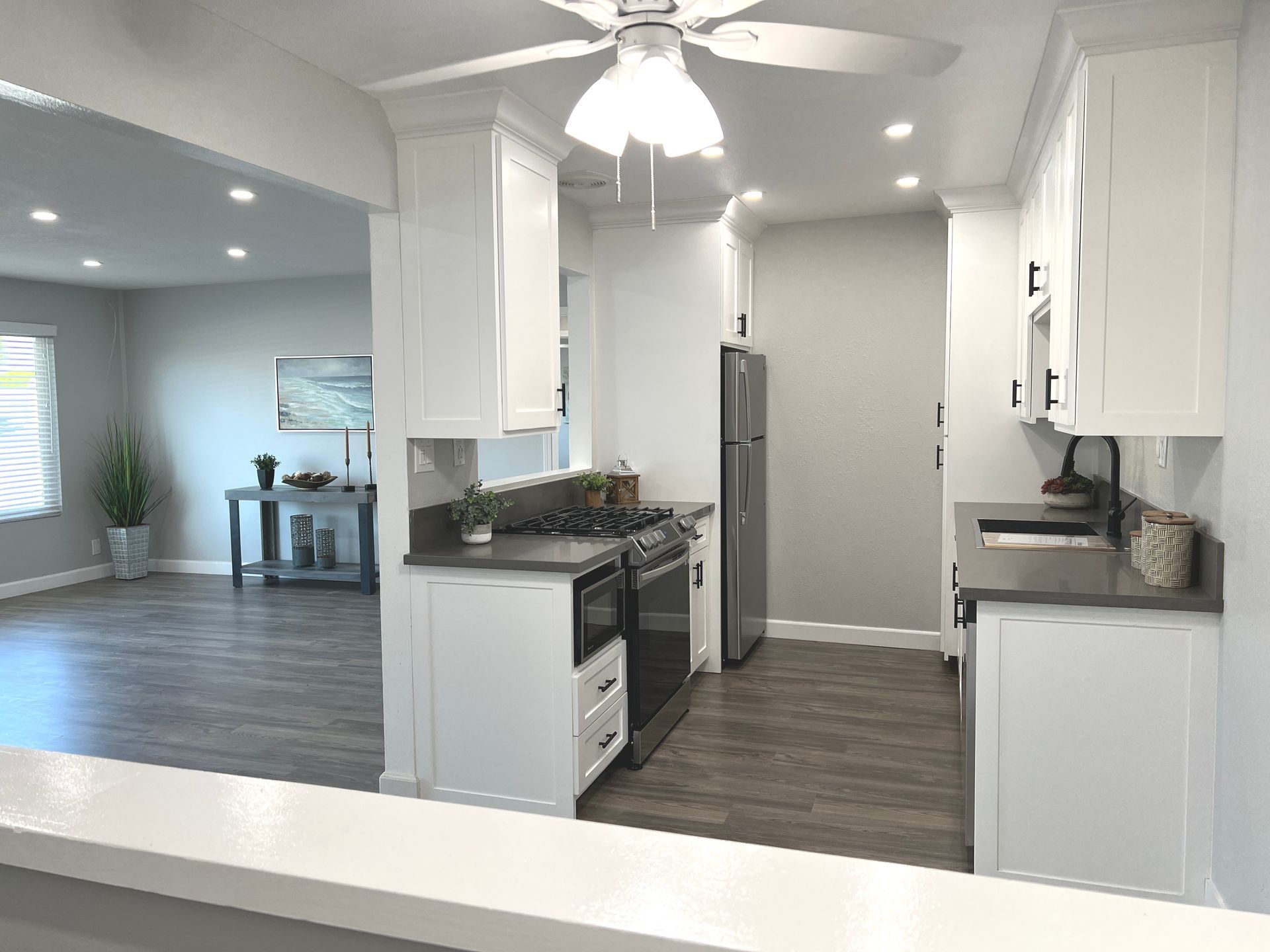 A kitchen with white cabinets , stainless steel appliances , and a ceiling fan.