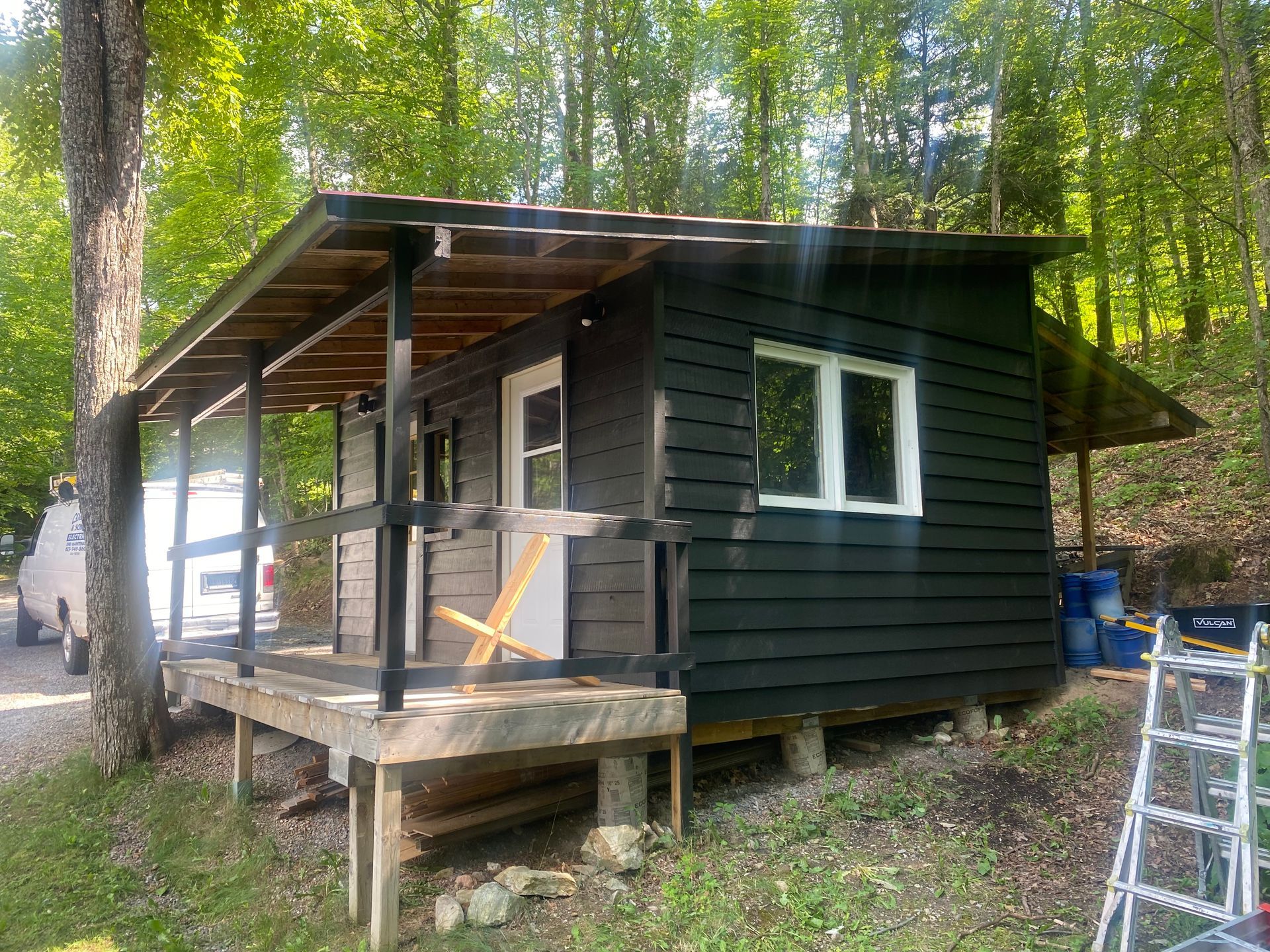 A small black house with a porch in the woods.