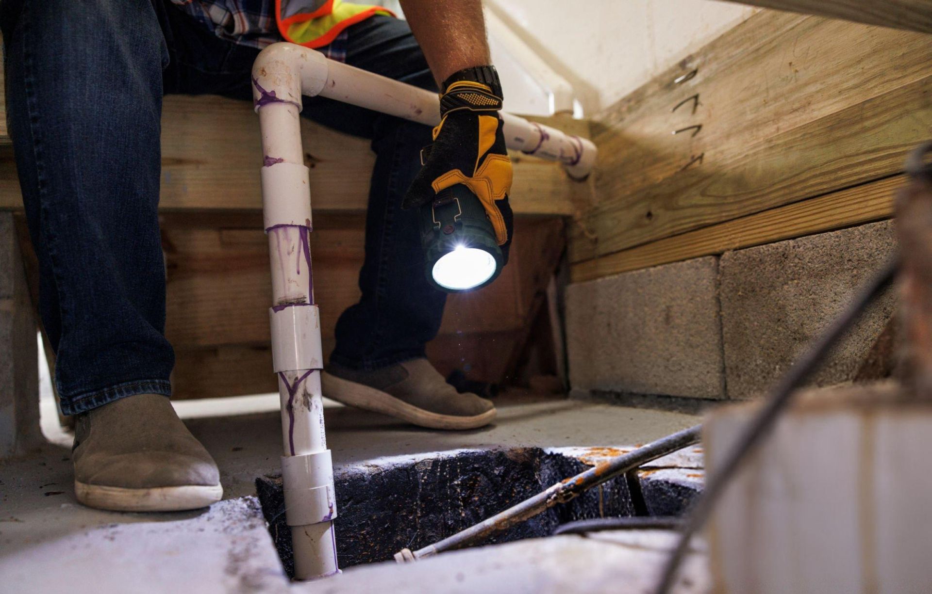 A worker is checking the sump pump with a flashlight.