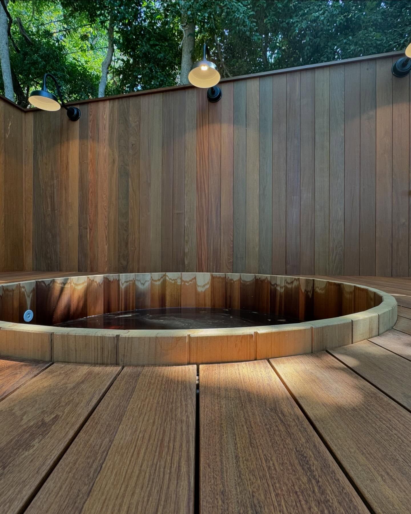 Wooden hot tub with lights and surrounding wood deck and fence.